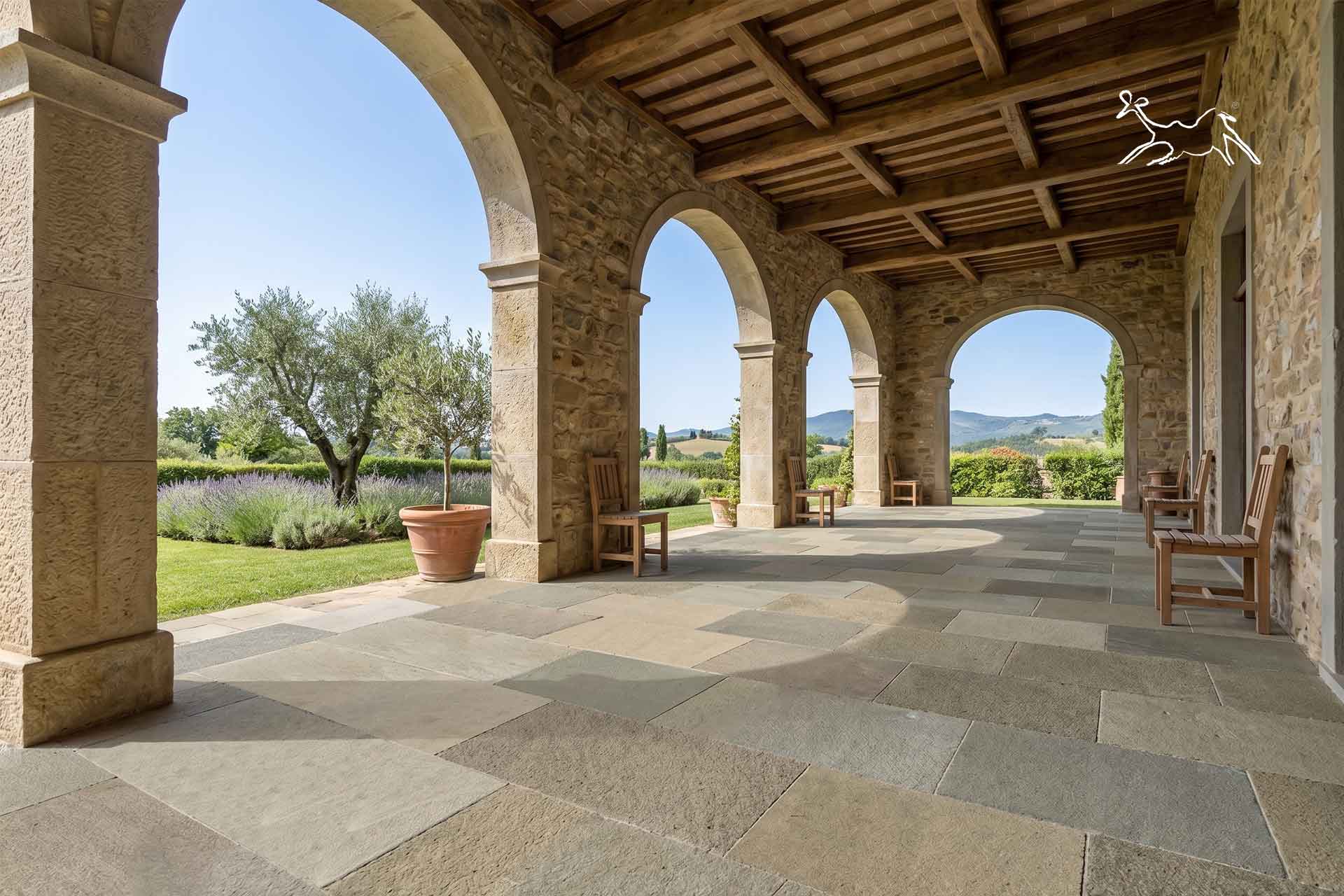 Pavimentazione in pietra naturale per portico esterno di villa in Toscana con archi in pietra, lastre in pietra naturale e finitura antiscivolo per terrazze e giardini.